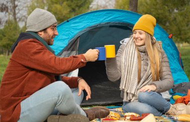 Kamp gezilerinde çadırlarının önünde fincanlarla kadeh kaldıran gülümseyen çift.