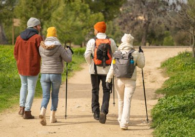 Dört yürüyüşçünün arka görüntüsü manzaralı bir doğa turunun keyfini çıkarıyor, sırt çantaları ve yürüyüş direkleriyle kirli bir yolda yürüyorlar