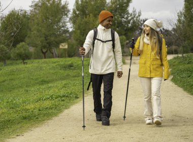 Irklar arası çiftler doğa yürüyüşünden zevk alıyorlar, yürüyüş direkleri ve gülümseme kullanarak.