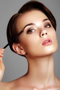 Güzel ve genç birbayan Vakfı yüzündeki gri arka plan üzerinde izole bir makyaj fırçası ile uygulama. Çekici genç beyaz modeli. Kozmetik toz yüzünde cilt bakım kavramı uygulama kız