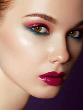 Kozmetik ürünleri. Neşeli genç kadının renkli makyaj ile kapatın. Kadın modeli ile menekşe arka plan üzerinde canlı makyaj Güzellik Portresi