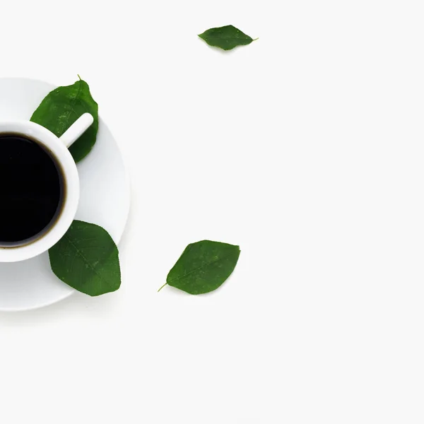 Piso tendido, escritorio de mesa de oficina con vista superior. Espacio de trabajo con hoja verde y taza de café sobre fondo blanco. Café negro fuerte en taza blanca. Vista superior, espacio para texto — Foto de Stock