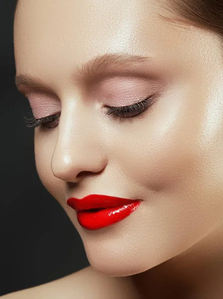 Muhteşem genç esmer kadın portresi. Mükemmel kaşlı, temiz makyajlı, kırmızı dudaklı, yüzüne dokunan güzel model kız. Parti için seksi bayan makyajı. Siyah arkaplanda izole