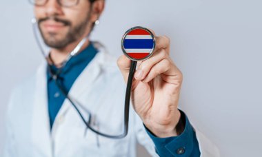 Doktor steteskopla Tayland bayrağını tutuyor. Tayland sağlık ve bakım konsepti, steteskopta Tayland bayrağı