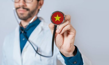 Doktor elinde steteskopla Vietnam bayrağı tutuyor. Vietnam sağlık ve bakım konsepti, steteskopta Vietnam bayrağı
