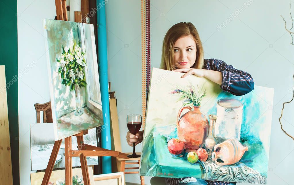 girl painter with a palette of colors and a glass of wine in an art studio. Palettes and easel, creative mood