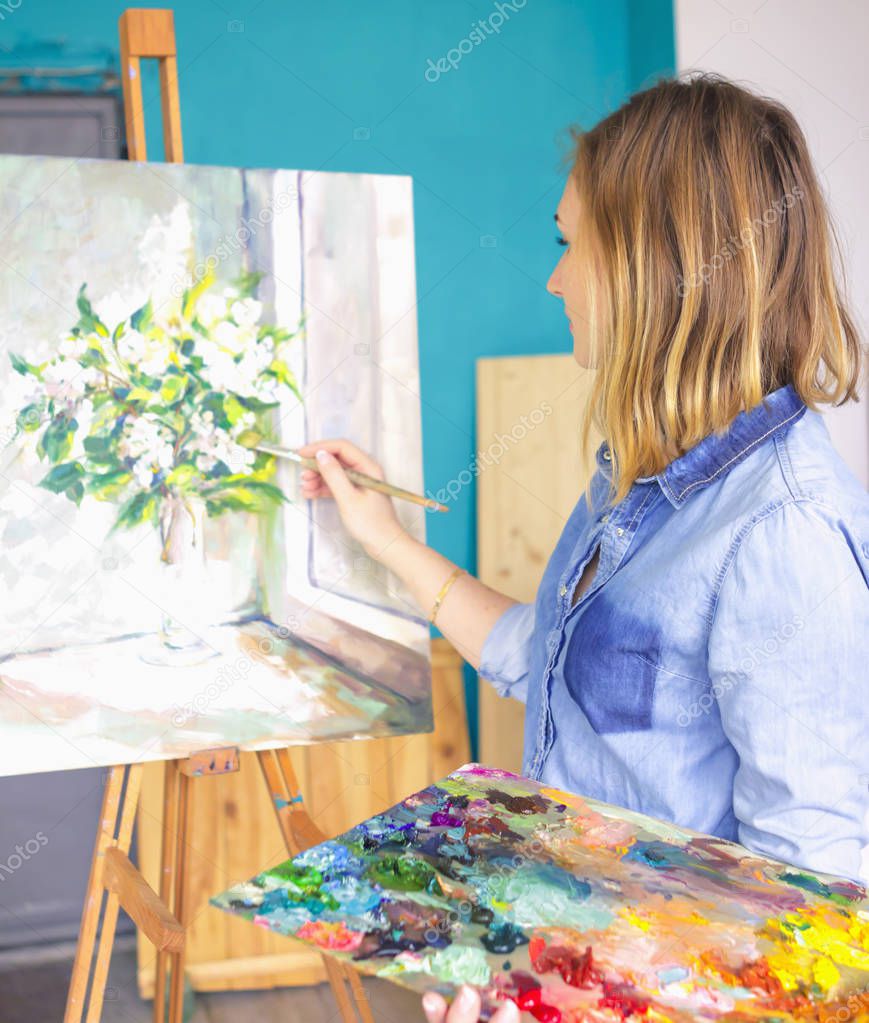 girl artist with a palette of paints draws paintings in an art studio. Palettes and easel, creative mood