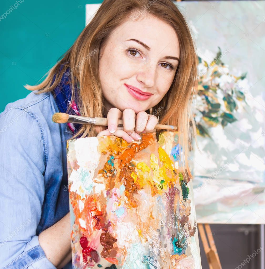 portrait of a girl painter with a palette of colorful paintings in an art studio. Thoughtful artist, creative mood