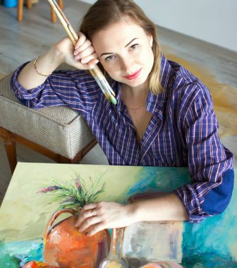 Elinde boya paleti olan bir kız sanatçı. Doğrudan kameraya bakıyor. Sanat stüdyosu