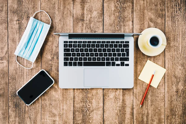 COVID salgını sırasında ofis çalışma alanı ve ofis masası. Yüz maskeli dizüstü bilgisayar çalışıyor.