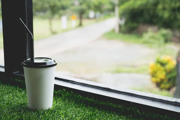 Iced coffee on green grass beside window blurred background