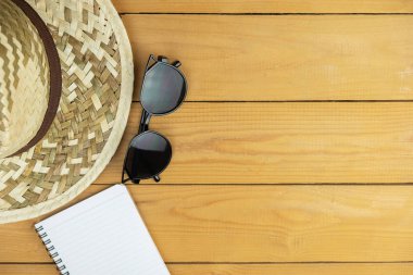 Kahverengi ahşap masa üzerinde dokuma şapkalı gözlük ve not defteri, seyahat ve tatil konsepti