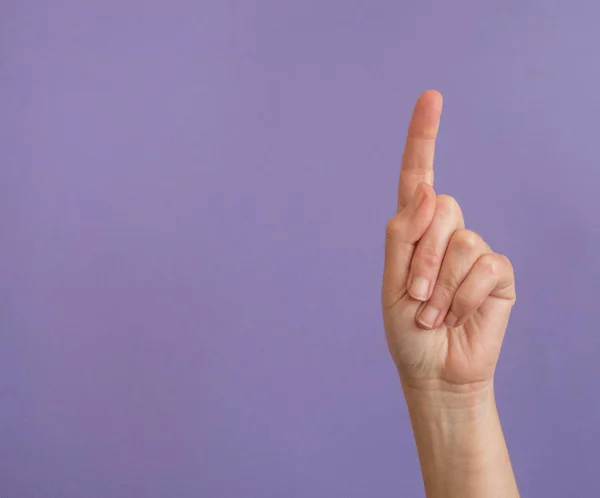 Hand with raised index finger on purple background with copy spa