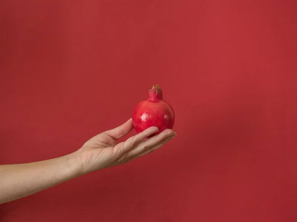コピースペース付きの赤い背景にザクロを持つ手 — ストック写真