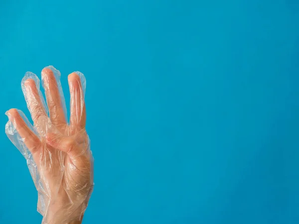 Hand with plastic glove with four fingers up on blue background with copy space