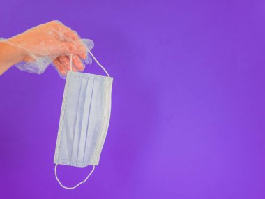 Ellerinde plastik eldiven, menekşe arkaplanda hijyenik maske ve kopyalama alanı var.