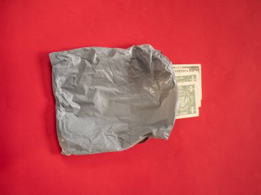 Kırmızı zemin üzerinde para olan gri plastik teslimat çantası.