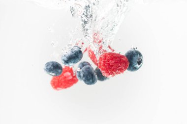 Blueberrys ve raspberrys kristal sıçramasına berrak su hava kabarcıkları ve batan beyaz arka plan ile