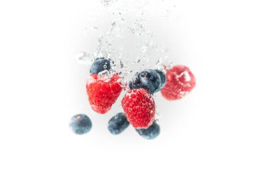Blueberrys ve raspberrys kristal sıçramasına berrak su hava kabarcıkları ve batan beyaz arka plan ile