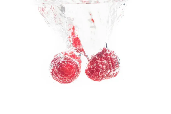 Zwei Himbeeren, die in die Wasseroberfläche spritzen und sinken. isoliert auf weißem Hintergrund, Splash Food Fotografie. — Stockfoto