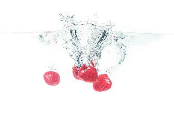 Bunch of raspberries splashing into water surface and sinking. Isolated on white background, splash food photography. — Stock Photo, Image