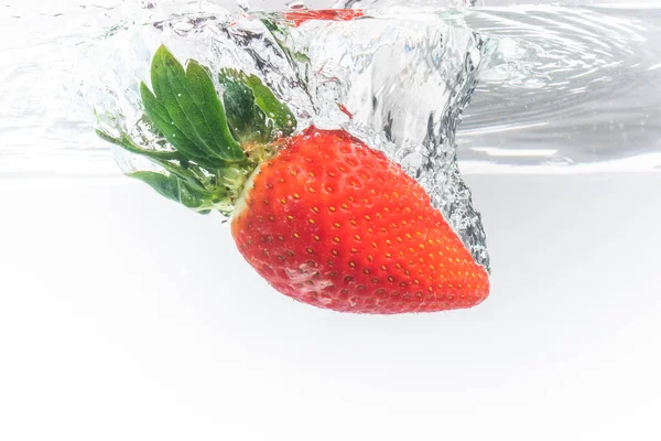 Fresa fresca cayó en agua clara con salpicadura aislada sobre fondo blanco . — Foto de Stock