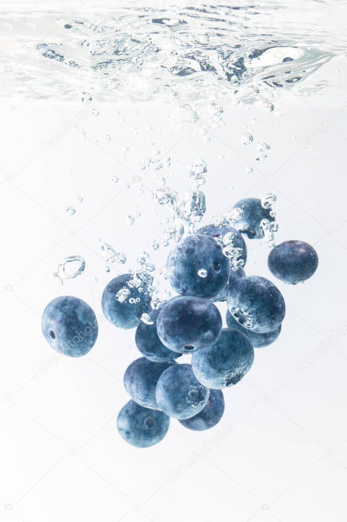 Bunch of blueberries splashing into water surface and sinking. Isolated on white background, splash food photography.