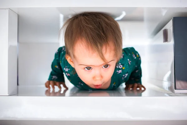 Cute caucasian baby girl crawl through tight space under coffee table towards camera