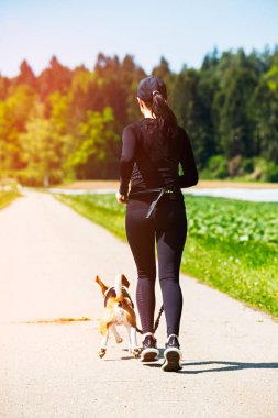 Sport girl is running with a dog (Beagle) on the rural road.