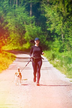 Sport girl is running with a dog (Beagle) on the rural road.