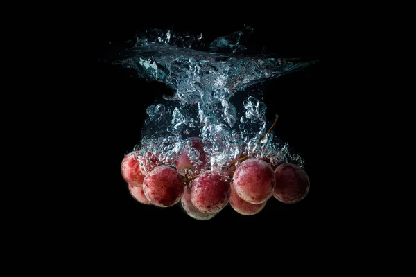 Rote Trauben planschen und versinken im Wasser auf schwarzem Hintergrund mit Luftblasen. — Stockfoto