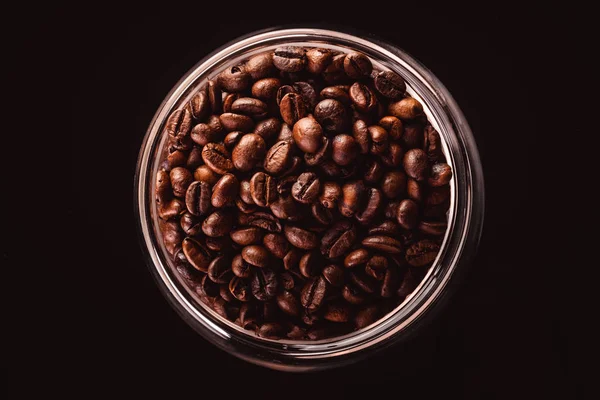 Coffee beans in glass jar standing on black background.