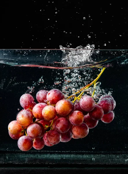 Izolált vörös szőlő fröccsenő és süllyedő vízben fekete alapon — Stock Fotó