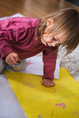 Balmumu pastel boyalı kağıdın üzerine iki yaşında bir çocuk resim çiziyor, içeride yerde oturuyor. Eğitim ve yaratıcılık geliştirme kavramı.