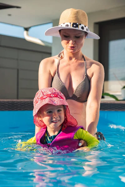 2-3 years old child with mother in swimming pool learn to swim. Baby in swimming west and red hat.Summer at home concept.