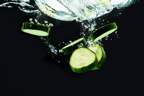 Sliced bio cucumber splashing water isolated on black background. Skin moisturizing cosmetics concept