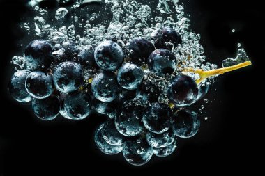Siyah arka planda izole edilmiş berrak suya sıçrayan kırmızı üzümler. Yemek sıçrama fotoğrafçılığı. Sağlıklı meyve teması.