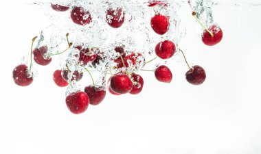 Kırmızı kirazlar kristal berrak suya hava kabarcıklarıyla sıçrıyor..