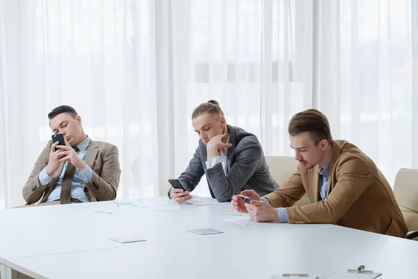 Aburrido hombres de negocios reunión ocioso buscando teléfono —  Fotos de Stock