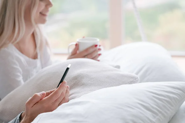 Jonggehuwden huwelijksreis plannen bed kopje smartphone — Stockfoto