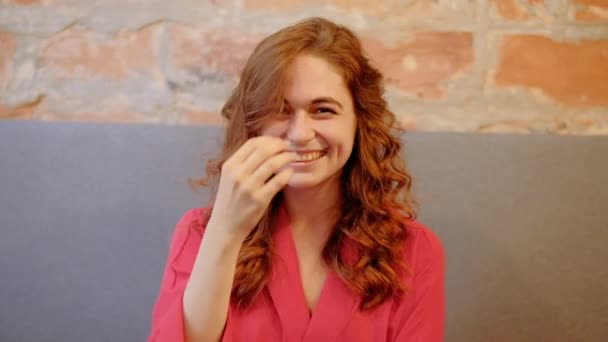 Кокетливая улыбающаяся женщина, играющая в кудрявые рыжие волосы — стоковое видео
