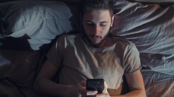 Álmatlan éjszaka unatkozó férfi olvasás takarmány telefon ágy — Stock videók