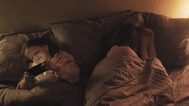 Дитина нічний телефон дівчина дивиться ліжко мама спить — стокове відео