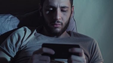 Uykusuz gece adamı çevrimiçi oyun telefon yatağı oynuyor.
