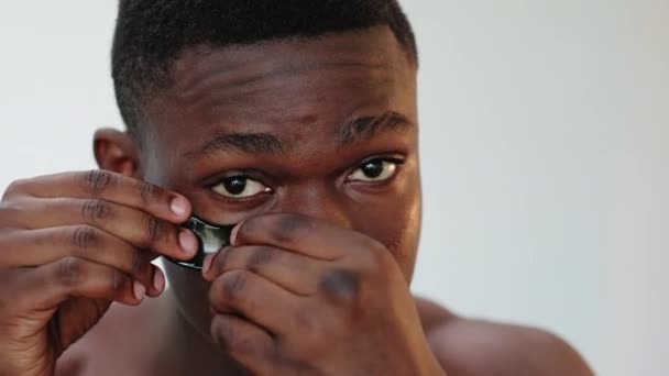 Hombre cuidado de la piel africano chico aplicando parche ojo negro — Vídeo de stock