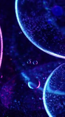 Dikey video. Yağ damlası. Hafif arkaplan. Bulanık mavi neon renkli su. Kimyasal doku sıvısı koyu renk sanat soyutlamasında daireler çiziyor..