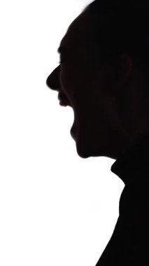 Dikey video. Çığlık atan siluet. Zihinsel bozukluk. Sinir krizi. Duygusal bir kriz. Beyazlar içinde izole bir şekilde bağıran, hayal kırıklığına uğramış bir kadının koyu renk karşıtlığı..