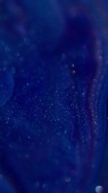 Dikey video. Mürekkep döküldü. Parlak lekeler. Bulanık mavi, mor renkli mermer rengi, emaye desenli, suda bulunan boya sıvısı soyut bokeh arka planda yayılıyor..