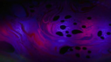 Floresan su mürekkebi. Bulanık spektrum sabunu. Renkli boya dalgası kıvrım sıvısı. Kırmızı menekşe floresan benzin soyut siyah arkaplan yüzüyor.