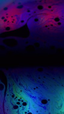 Dikey video. Sabun boyası. Holografik küre. Yağlı renkli neon akışı, yuvarlak sanat sıvısı noktasında. Kara geceyle ilgili soyut kozmik pigment sızıntısı.